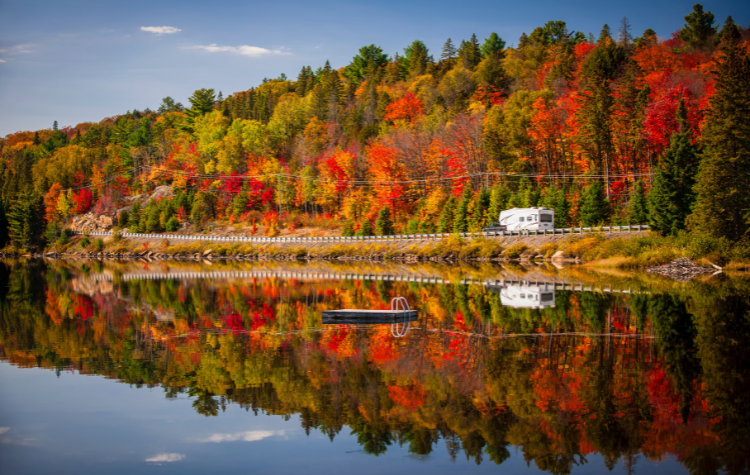 Bos met herfstkleuren en weg met camper refelcteren op Lake of Two Rivers, Algonquin Park, Ontario, Canada