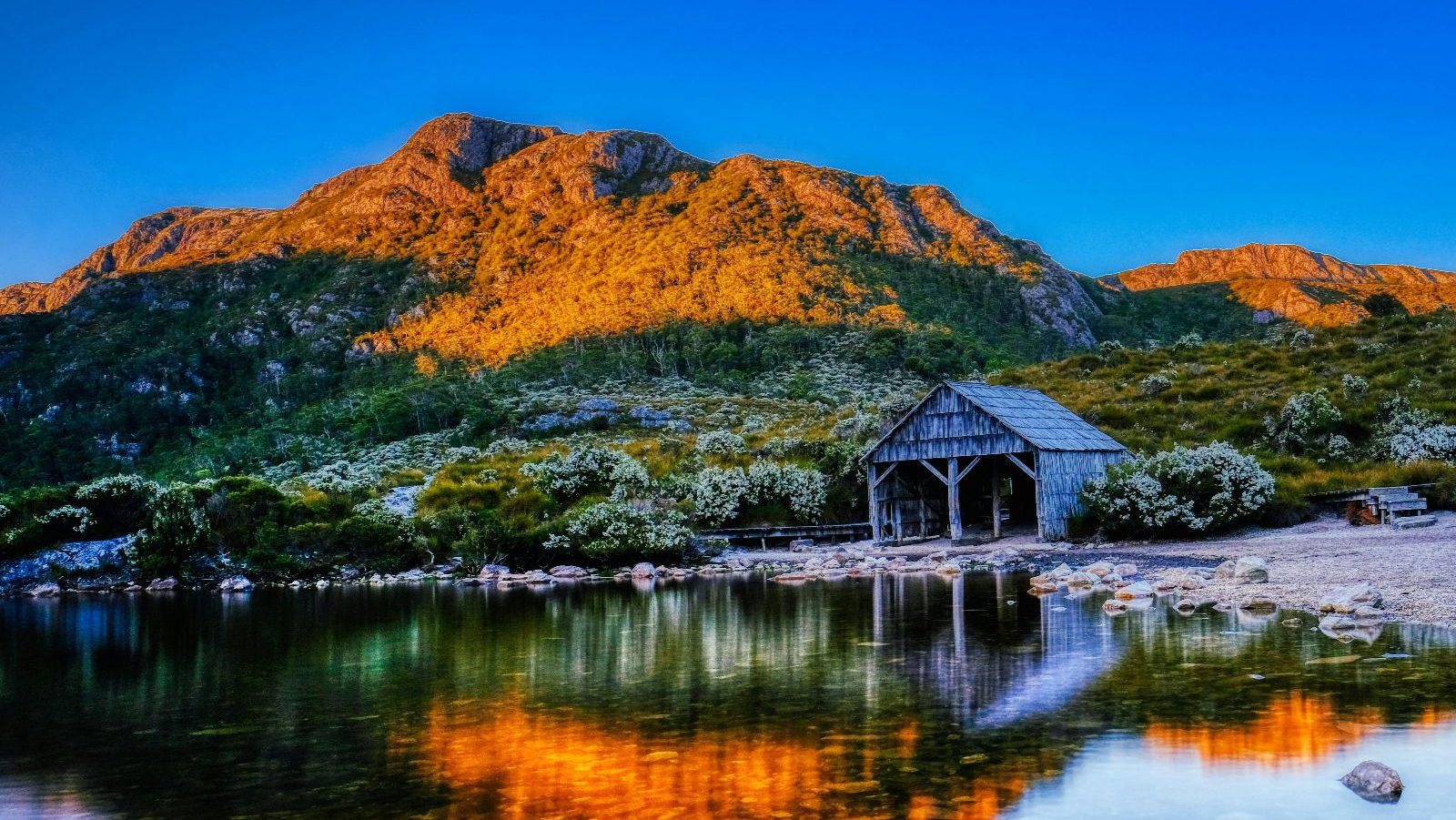 Rondreis Australië, Cradle Mountain National Park, Bergen met meer en hutje in de zon
