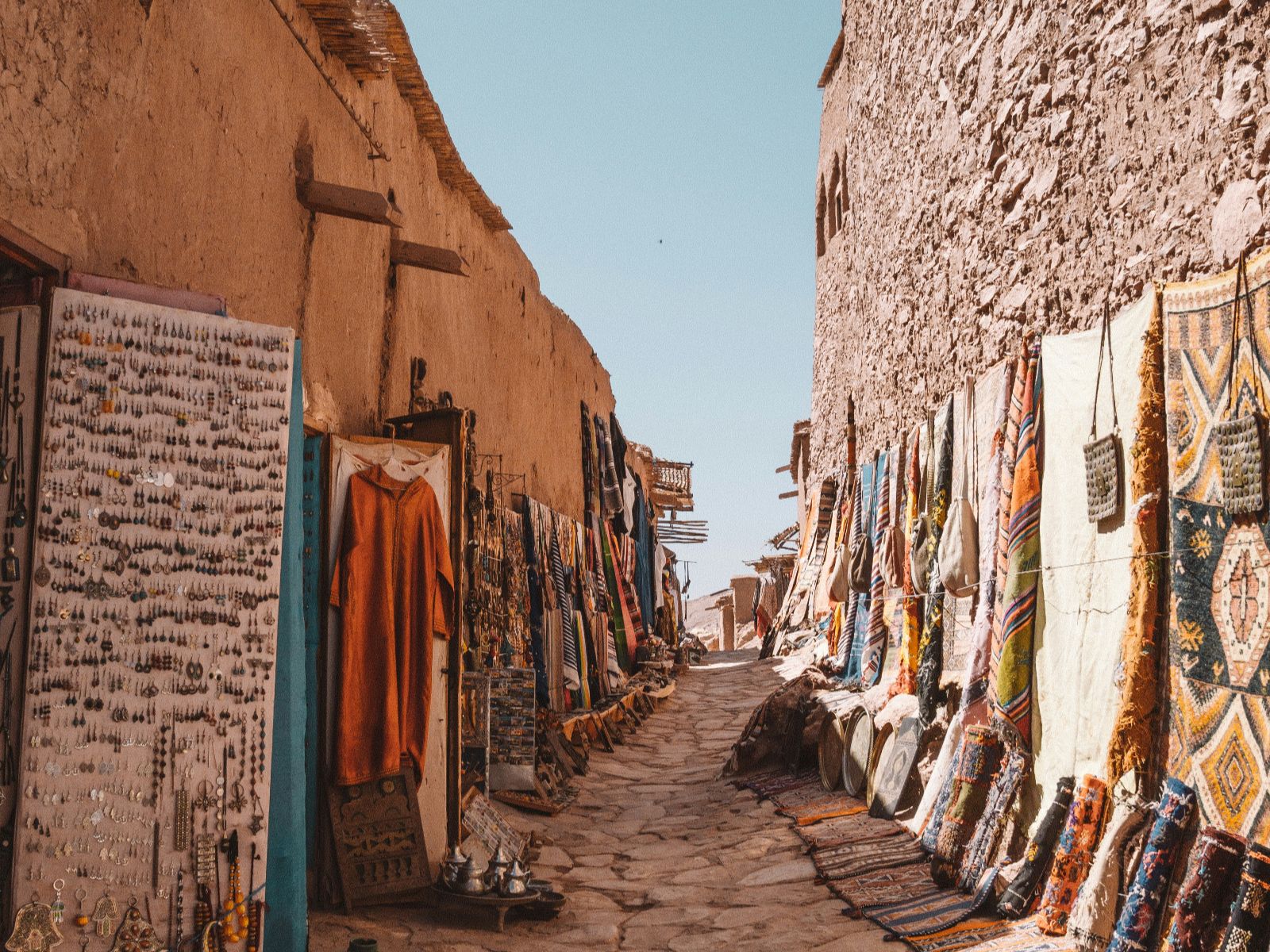 Rondreis Marokko, Aït Ben Haddou, straat met winkels met kledendracht en tapijten
